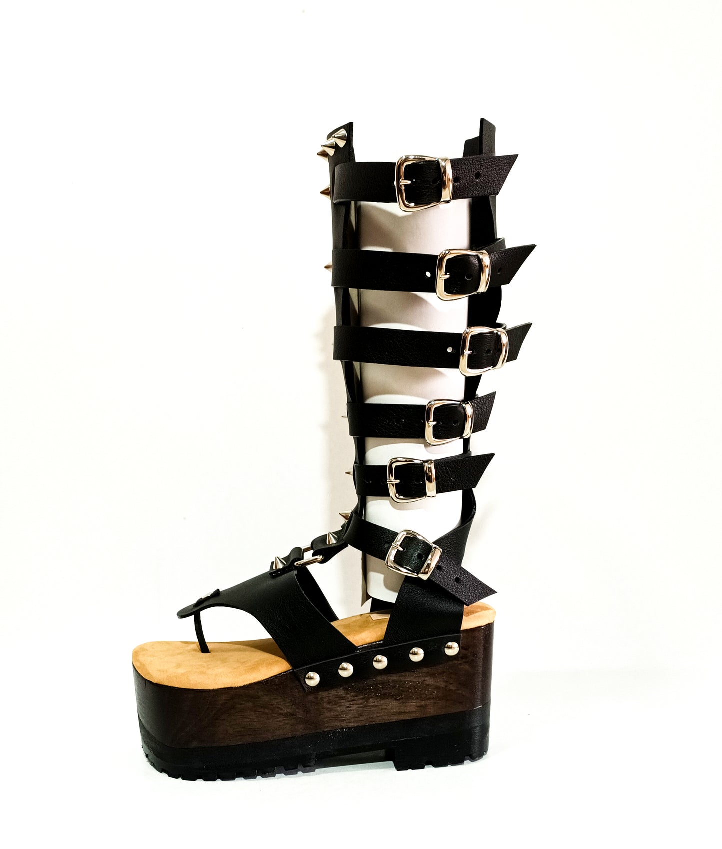 Vista lateral de las sandalias gladiadoras de cuero negro con suela de madera de wengué y tacón alto.