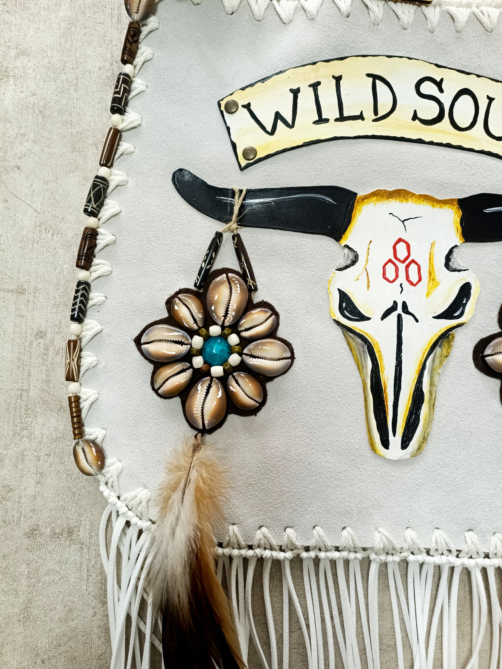 Bohemian-style white leather bag. Handmade leather bag with hand-painted buffalo decorated with shells, feathers, carved horn, and felcos. Handmade leather bag by Sol Caleyo.