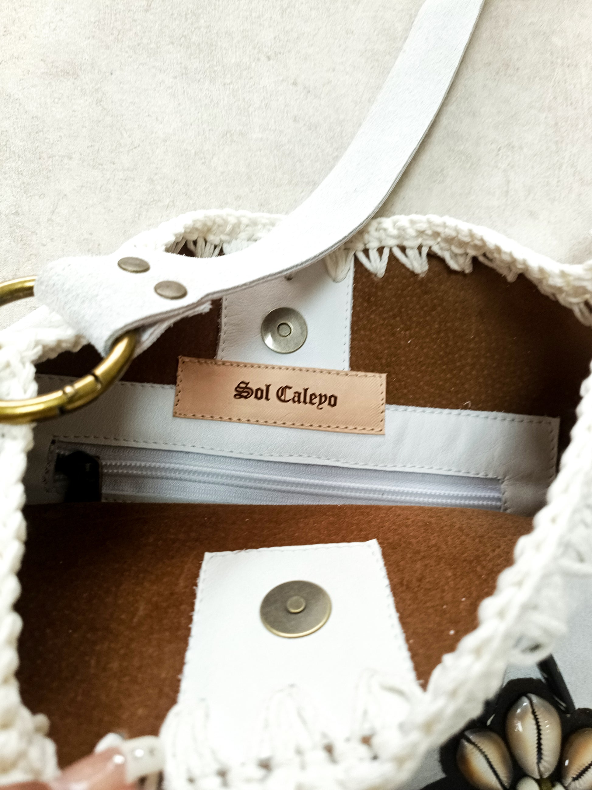Bohemian-style white leather bag. Handmade leather bag with hand-painted buffalo decorated with shells, feathers, carved horn, and felcos. Handmade leather bag by Sol Caleyo.