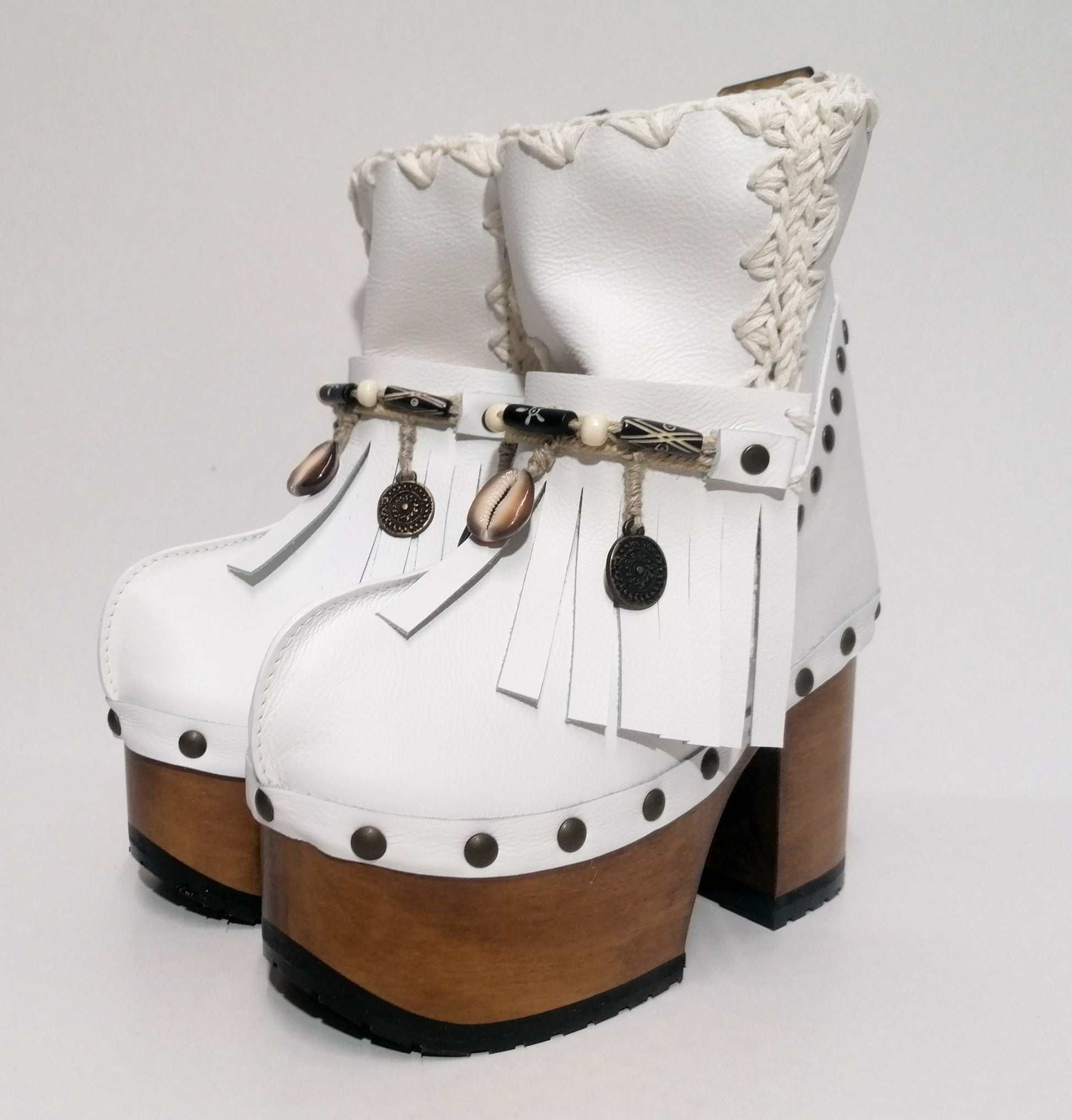 White leather clog boot. White leather boho style clog boot. White leather boot decorated with fringes, shells, coins and carved bone with a unique boho style. Super high heeled wooden boots 70's style. Sizes 34 to 47. High quality handmade leather shoes by sol Caleyo. Sustainable fashion.