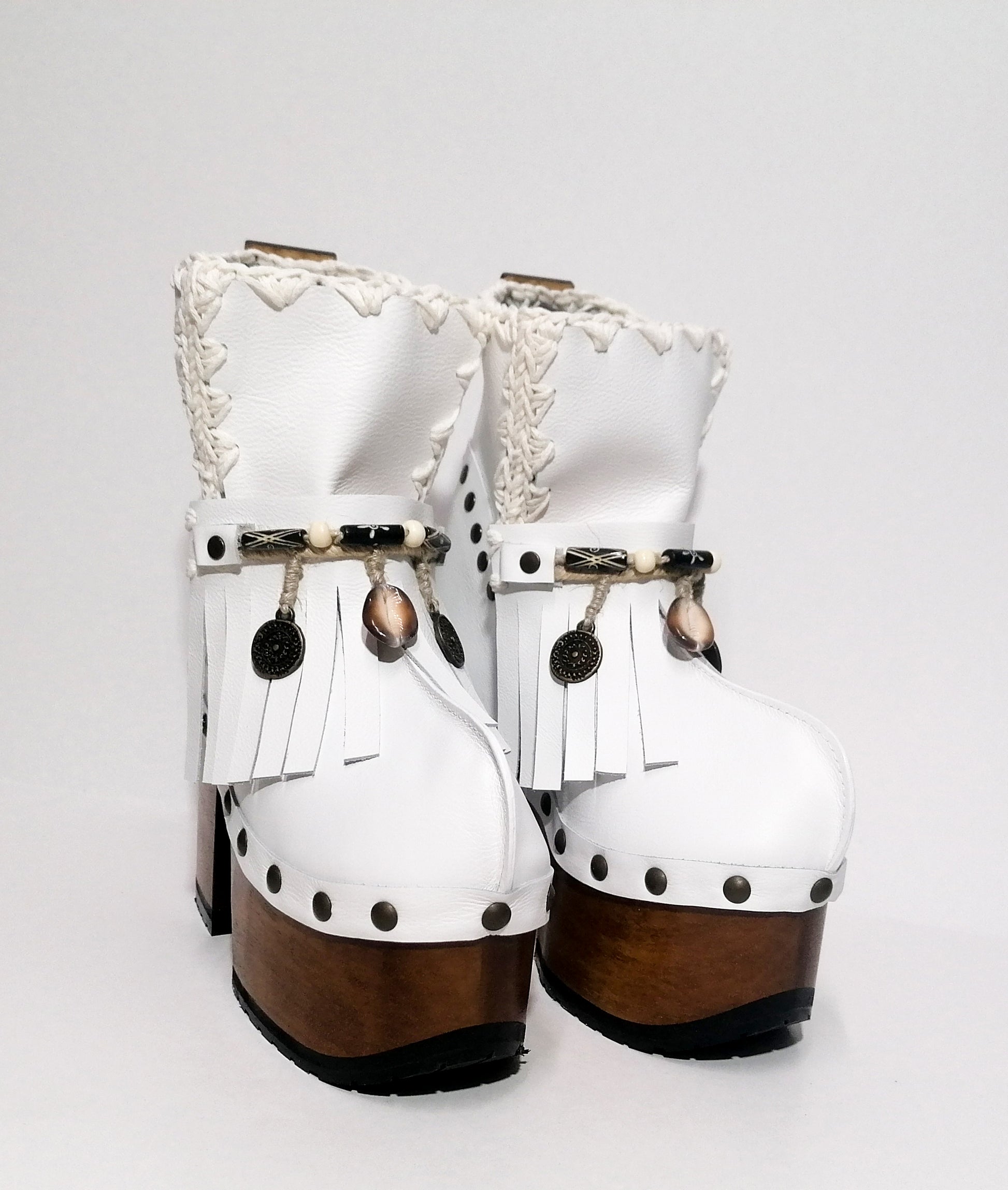 White leather clog boot. White leather boho style clog boot. White leather boot decorated with fringes, shells, coins and carved bone with a unique boho style. Super high heeled wooden boots 70's style. Sizes 34 to 47. High quality handmade leather shoes by sol Caleyo. Sustainable fashion.