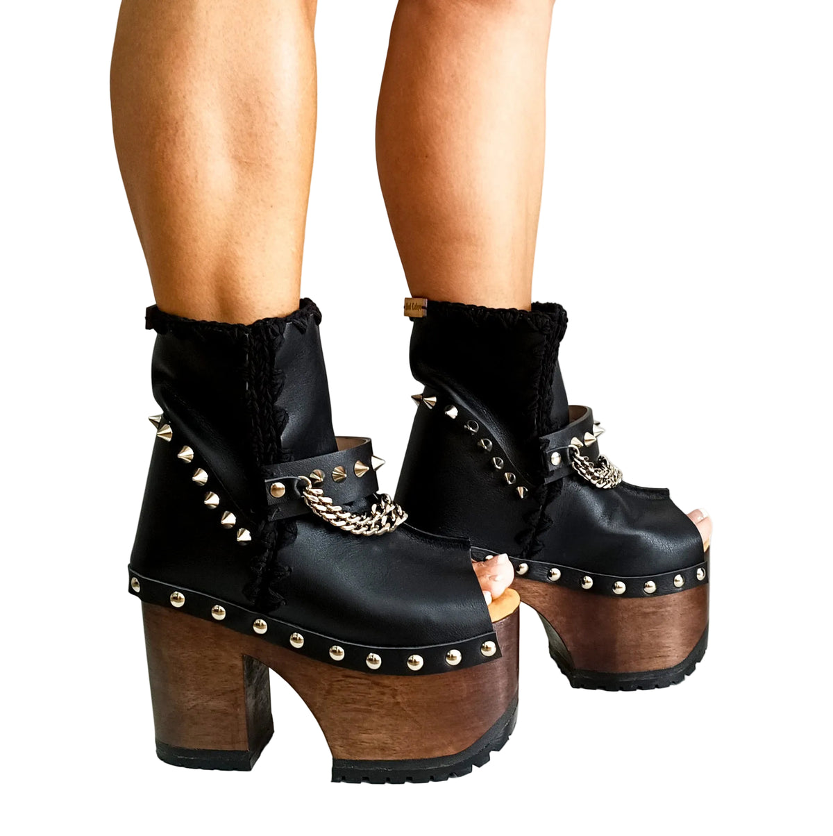 Handmade smooth black leather peep toe platform ankle boots with silver pyramid studs, front chains and 13 cm wenge lacquered wooden heel by Sol Caleyo.