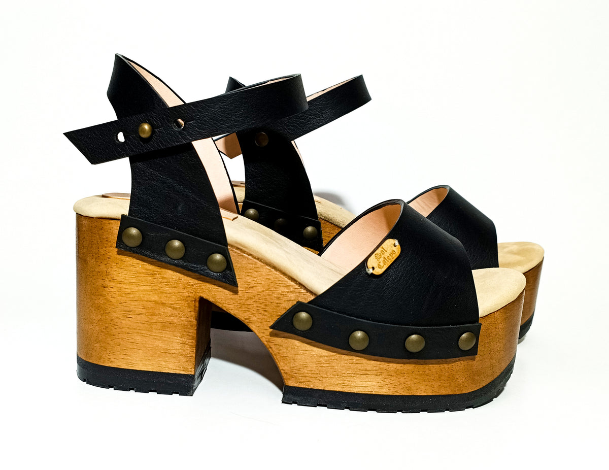 Handmade smooth black leather platform sandals with wide ankle strap and 8 cm natural lacquered wooden heel by Sol Caleyo .