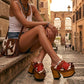 Fashion model wearing Verona Clogs with 12 cm wooden heels and cow print leather, styled in a historic European setting to showcase the vintage bohemian aesthetic.