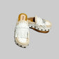 Handmade Niza Moccasin Clogs in white leather with beige crochet trim, leather fringes, and bronze studs on a wooden platform with a beige tractor sole.