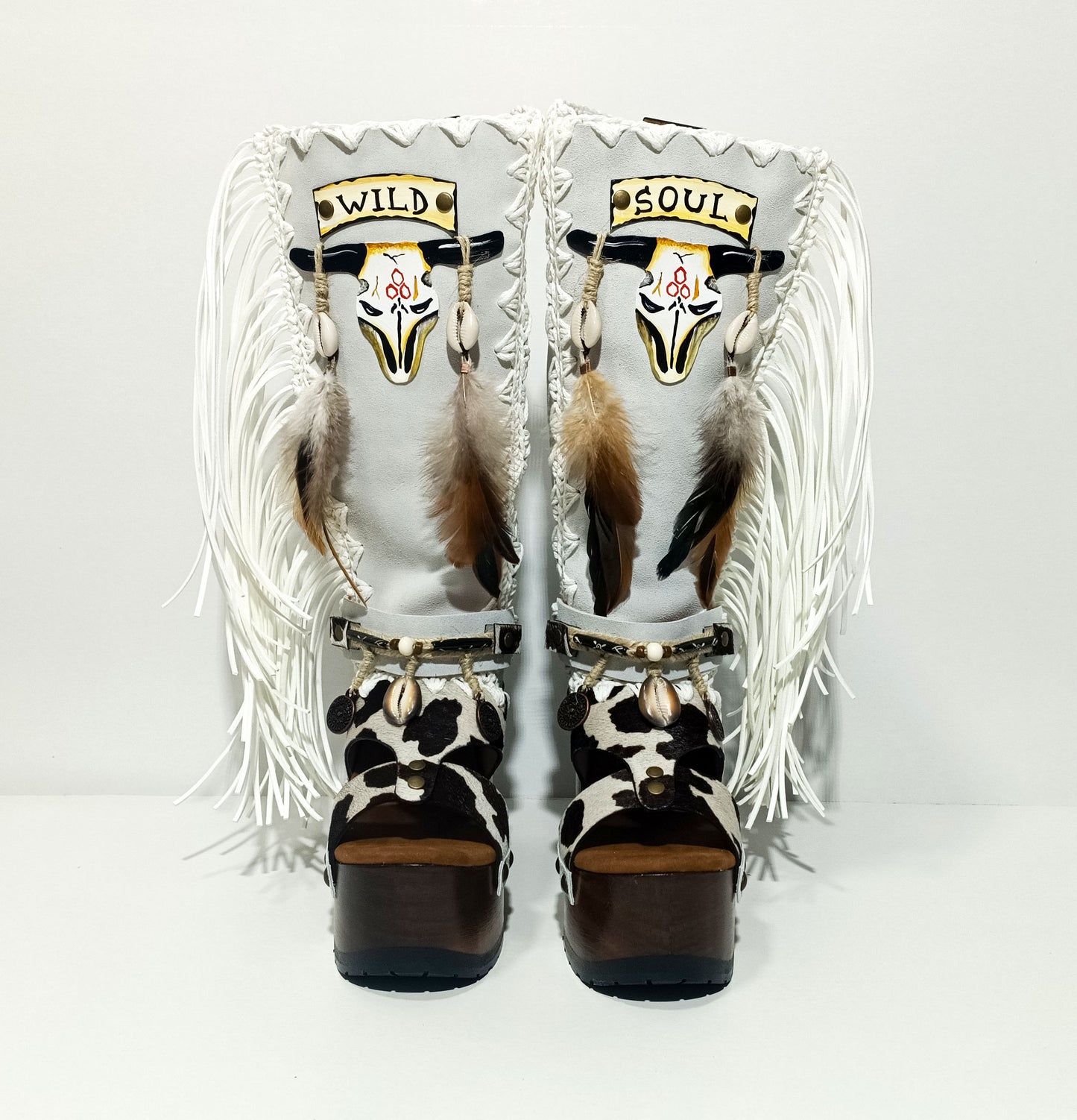 Handmade cowboy boots, white boots with cowhide and fringes. Cowboy style boots with hand painted buffalo, feathers, coins and natural shells. Vintage style platform boots. High-end leather footwear handmade by Sol Caleyo.