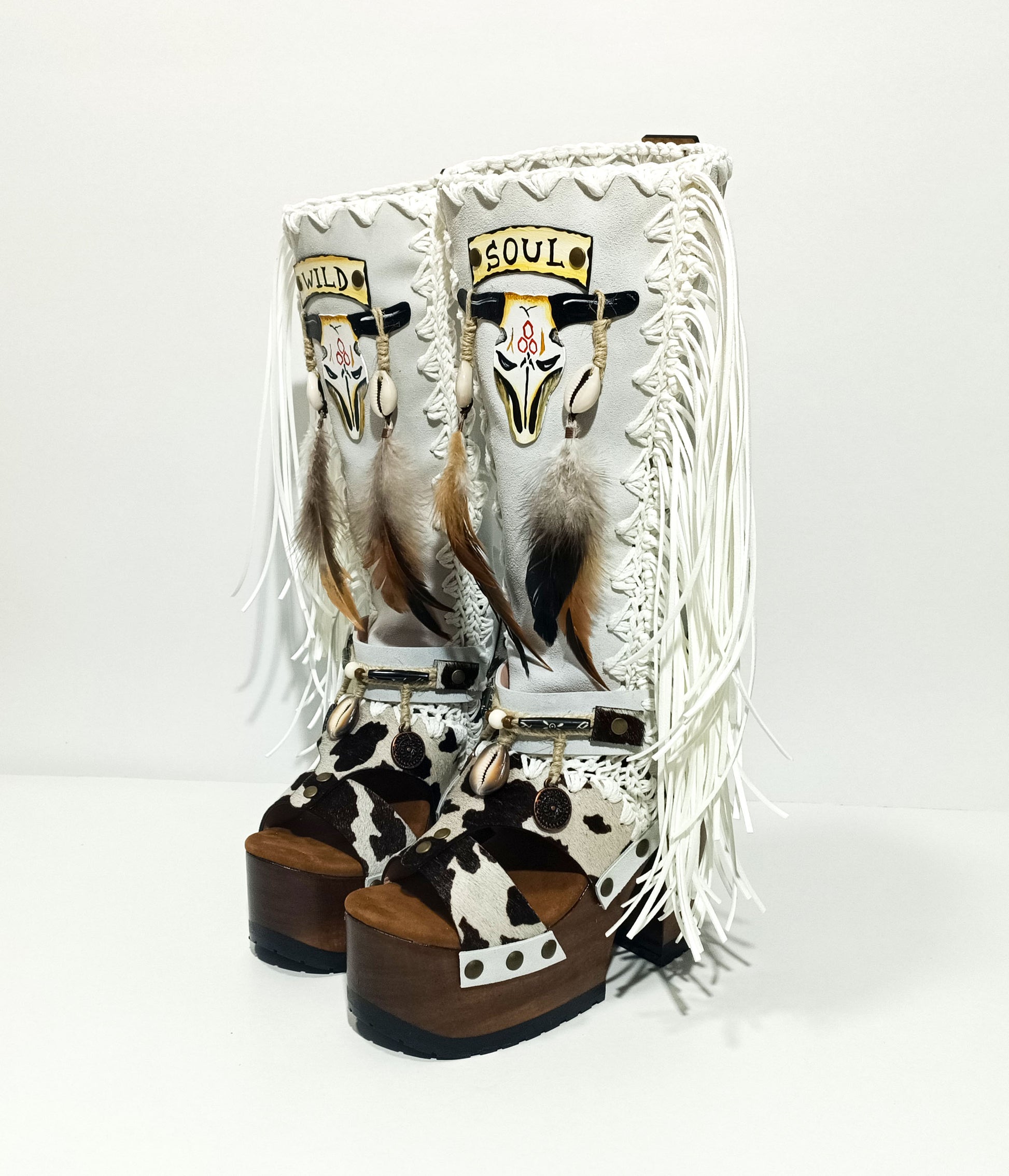 Handmade cowboy boots, white boots with cowhide and fringes. Cowboy style boots with hand painted buffalo, feathers, coins and natural shells. Vintage style platform boots. High-end leather footwear handmade by Sol Caleyo.