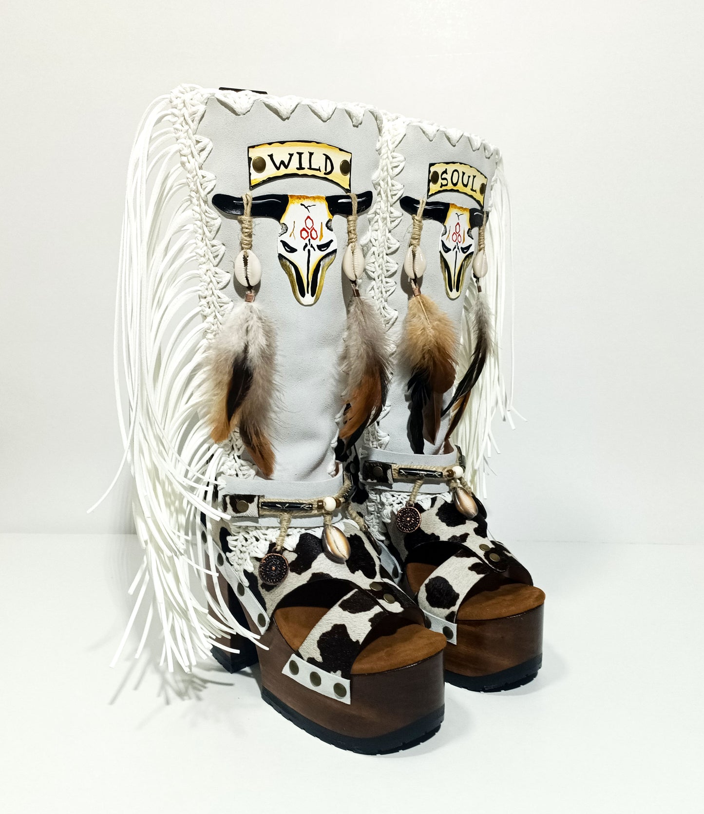 Handmade cowboy boots, white boots with cowhide and fringes. Cowboy style boots with hand painted buffalo, feathers, coins and natural shells. Vintage style platform boots. High-end leather footwear handmade by Sol Caleyo.