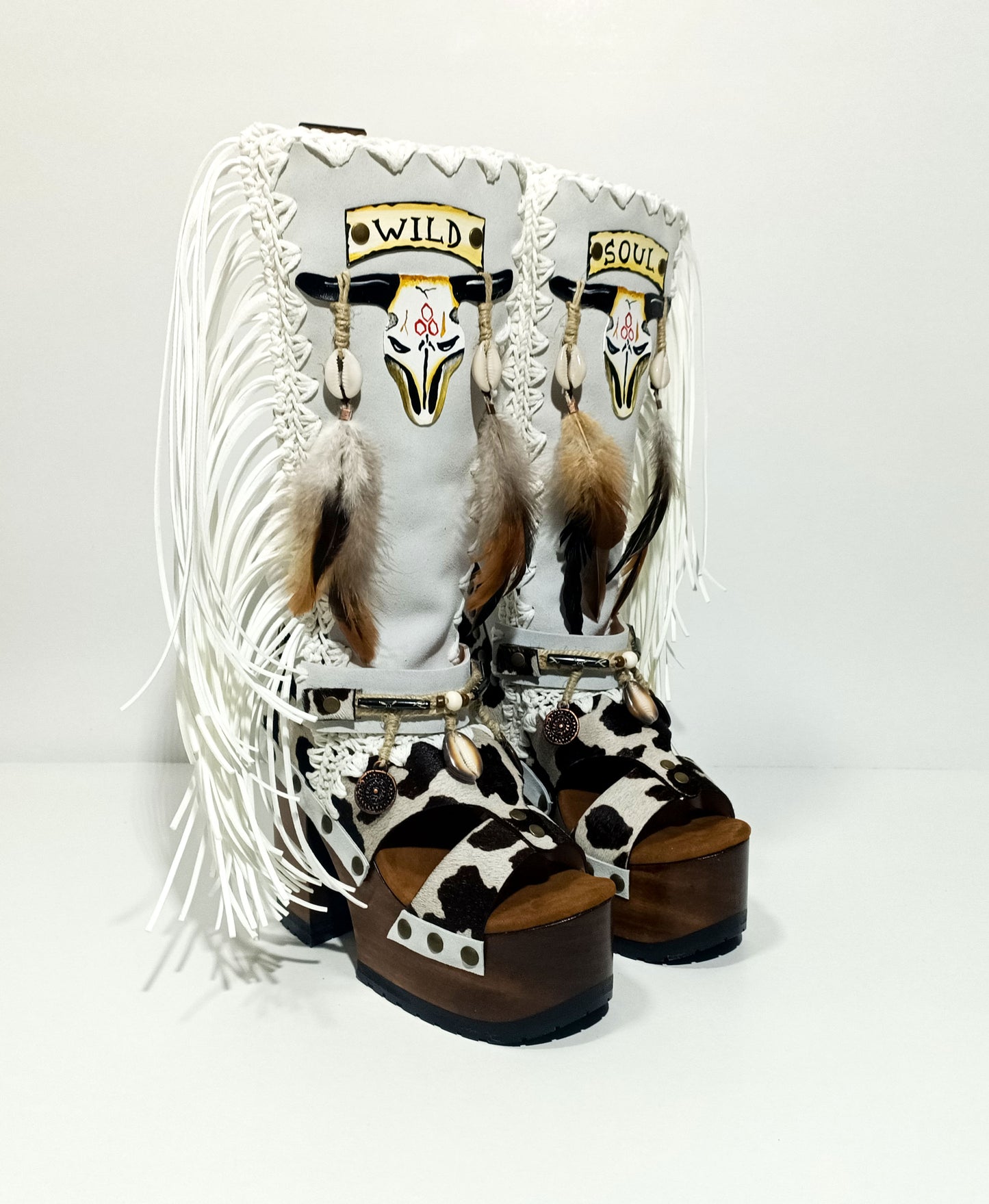 Handmade cowboy boots, white boots with cowhide and fringes. Cowboy style boots with hand painted buffalo, feathers, coins and natural shells. Vintage style platform boots. High-end leather footwear handmade by Sol Caleyo.