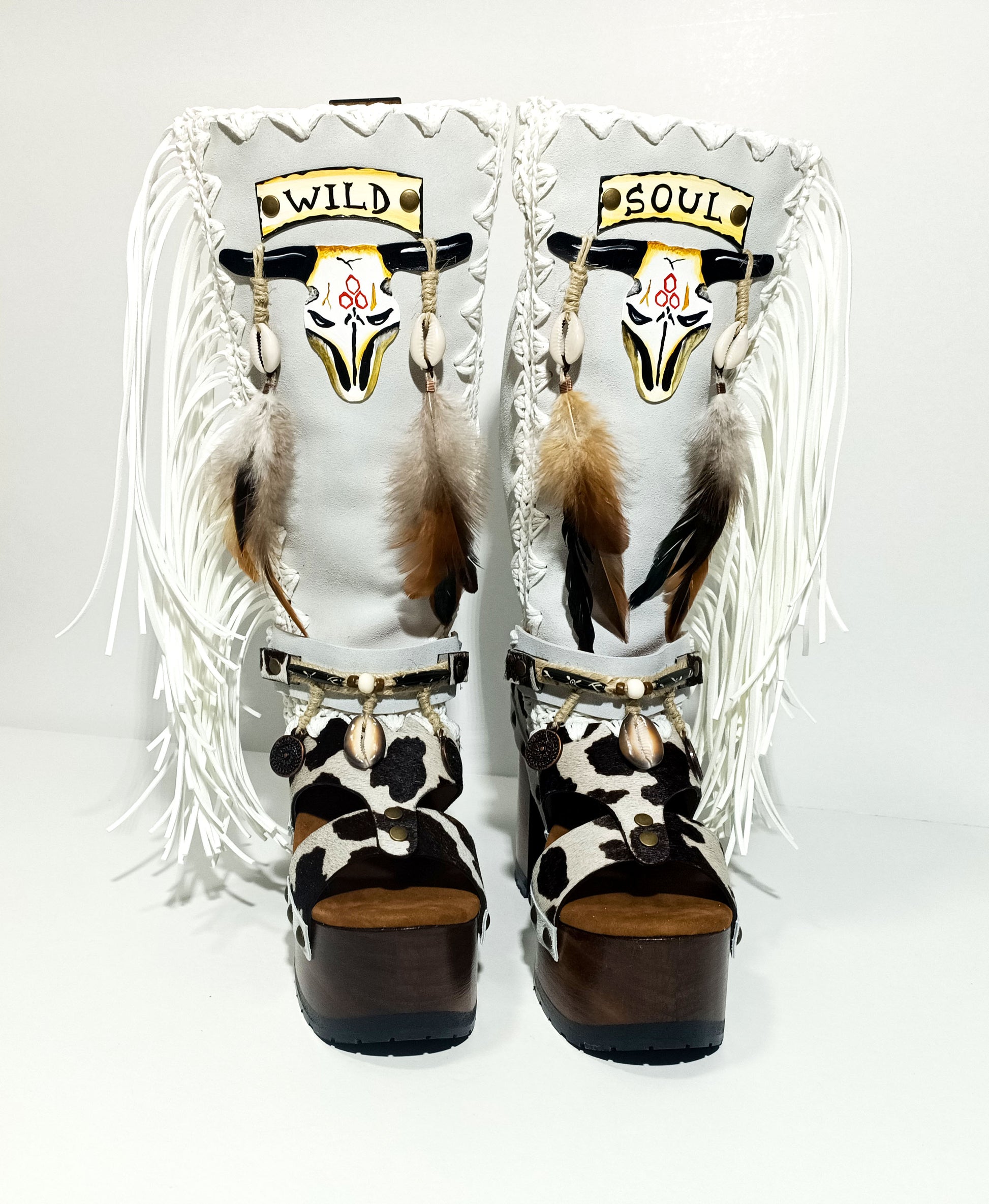 Handmade cowboy boots, white boots with cowhide and fringes. Cowboy style boots with hand painted buffalo, feathers, coins and natural shells. Vintage style platform boots. High-end leather footwear handmade by Sol Caleyo.