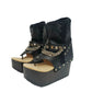 Sol Caleyo Texas Boots: Handcrafted black leather platform flip-flop sandals with wooden wedge heel, silver pyramid studs, and decorative chains. 9cm heel with zig-zag rubber traction sole.
