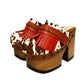 Verona Clogs by Sol Caleyo featuring light brown cow hair leather, red fringe details, and old gold studs on a high wooden platform sole with tractor grip.