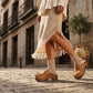 Sol Caleyo Niza Moccasin Clogs in light brown leather worn on a cobblestone street, featuring crochet details, fringes, and a wooden platform sole