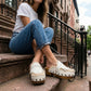 Model wearing white Niza Moccasin Clogs by Sol Caleyo, styled with blue jeans and a white t-shirt for a classic urban bohemian look on city steps.