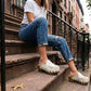 Model wearing white Niza Moccasin Clogs by Sol Caleyo, styled with blue jeans and a white t-shirt for a classic urban bohemian look on city steps.