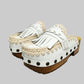 Handmade Niza Moccasin Clogs in white leather with beige crochet trim, leather fringes, and bronze studs on a wooden platform with a beige tractor sole.