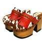 Verona Clogs by Sol Caleyo featuring light brown cow hair leather, red fringe details, and old gold studs on a high wooden platform sole with tractor grip.