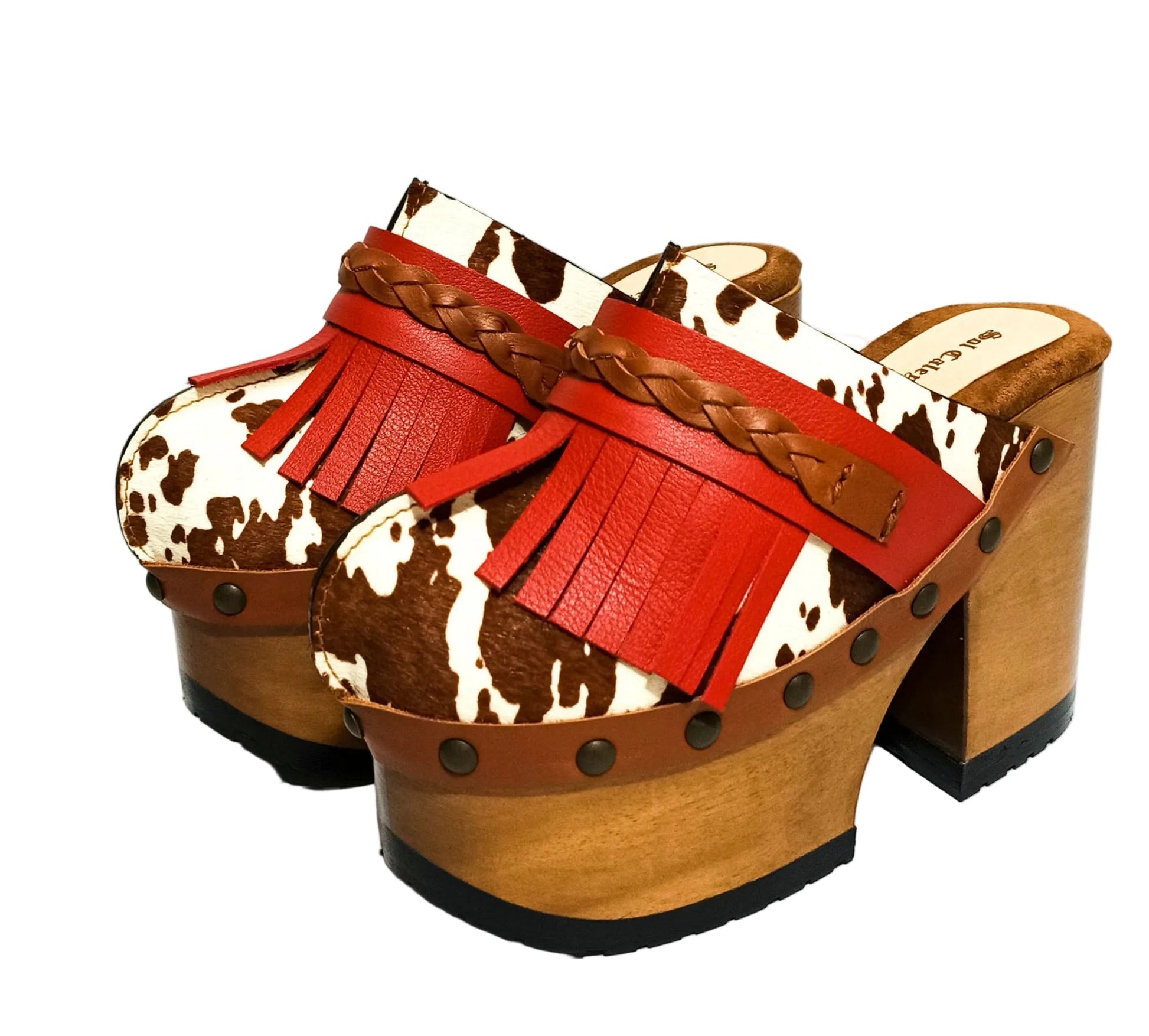 Verona Clogs by Sol Caleyo featuring light brown cow hair leather, red fringe details, and old gold studs on a high wooden platform sole with tractor grip.