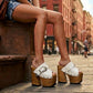 Model wearing custom-made White Western Sandals, highlighting the artisanal wood craftsmanship and extreme platform height in an urban setting.