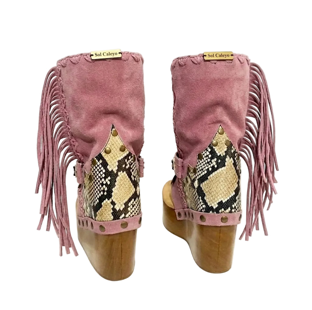 Handmade Atenea Pink Flip Flop Boots by Sol Caleyo, featuring pink suede leather, fringe details, shells, vintage coins, and a high wooden platform sole on a white background