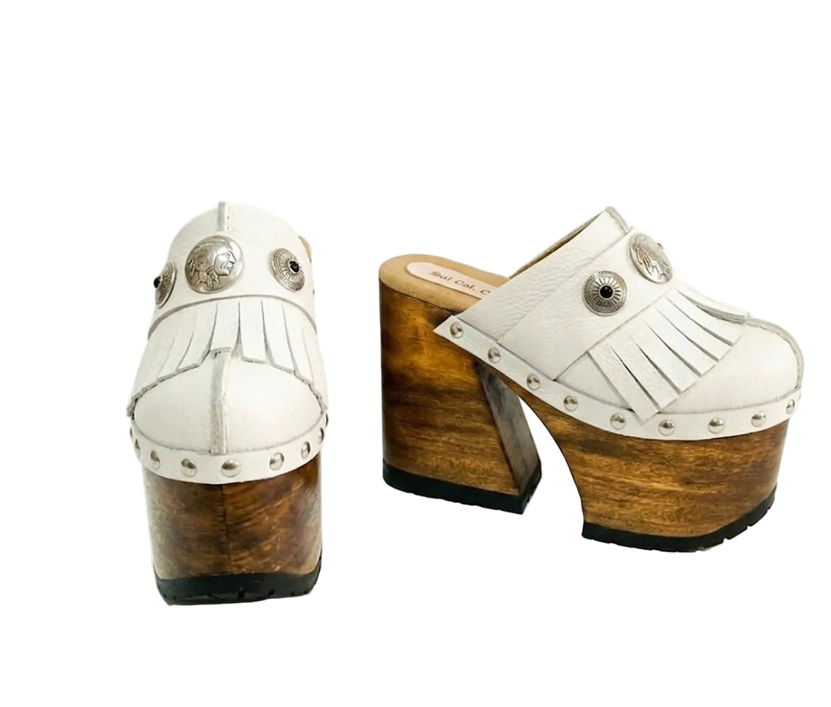 Side view of White Indian Clogs XL featuring extreme 17cm natural wood platform, white leather fringes, and antique silver metal conchos.