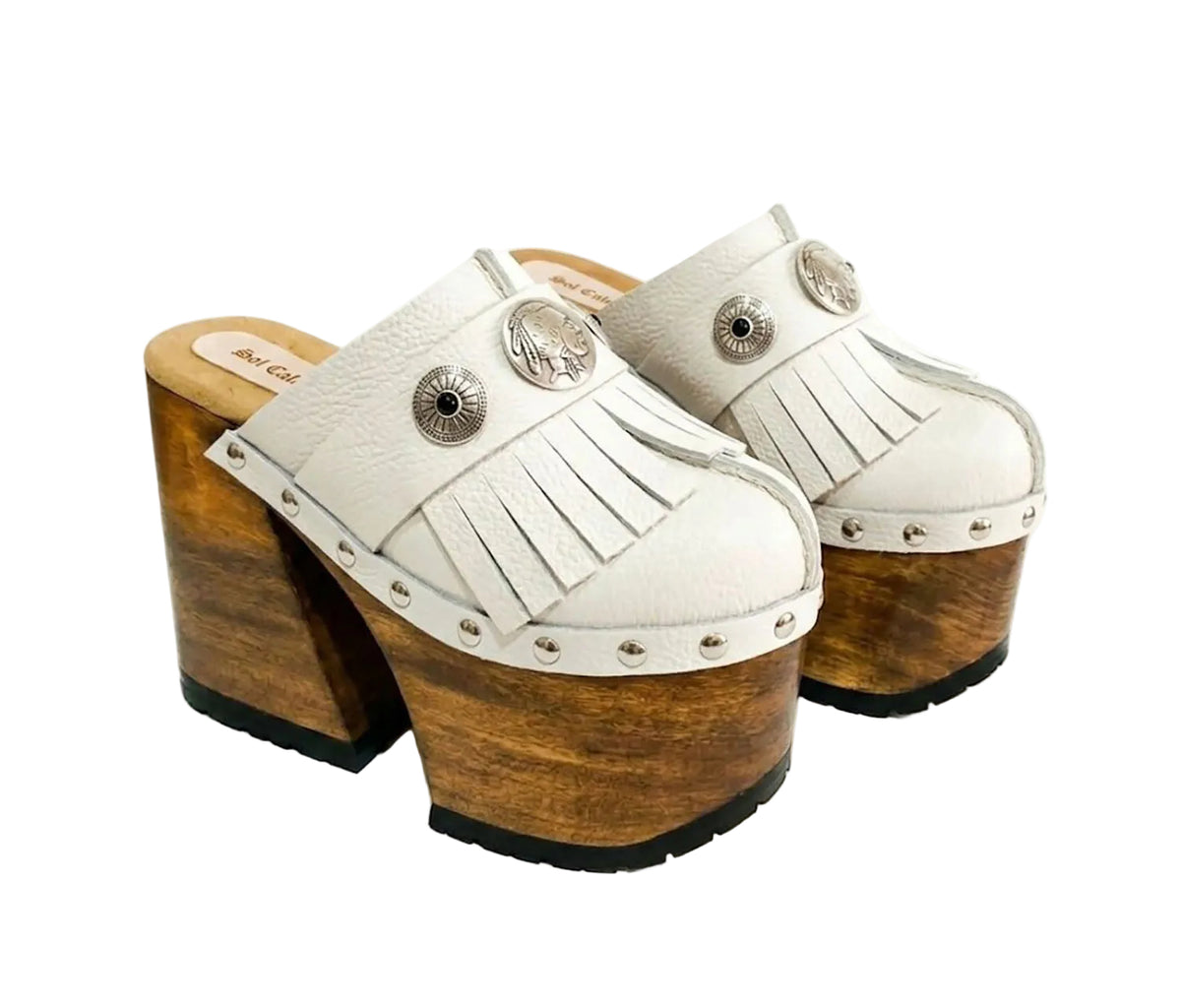 Side view of White Indian Clogs XL featuring extreme 17cm natural wood platform, white leather fringes, and antique silver metal conchos.