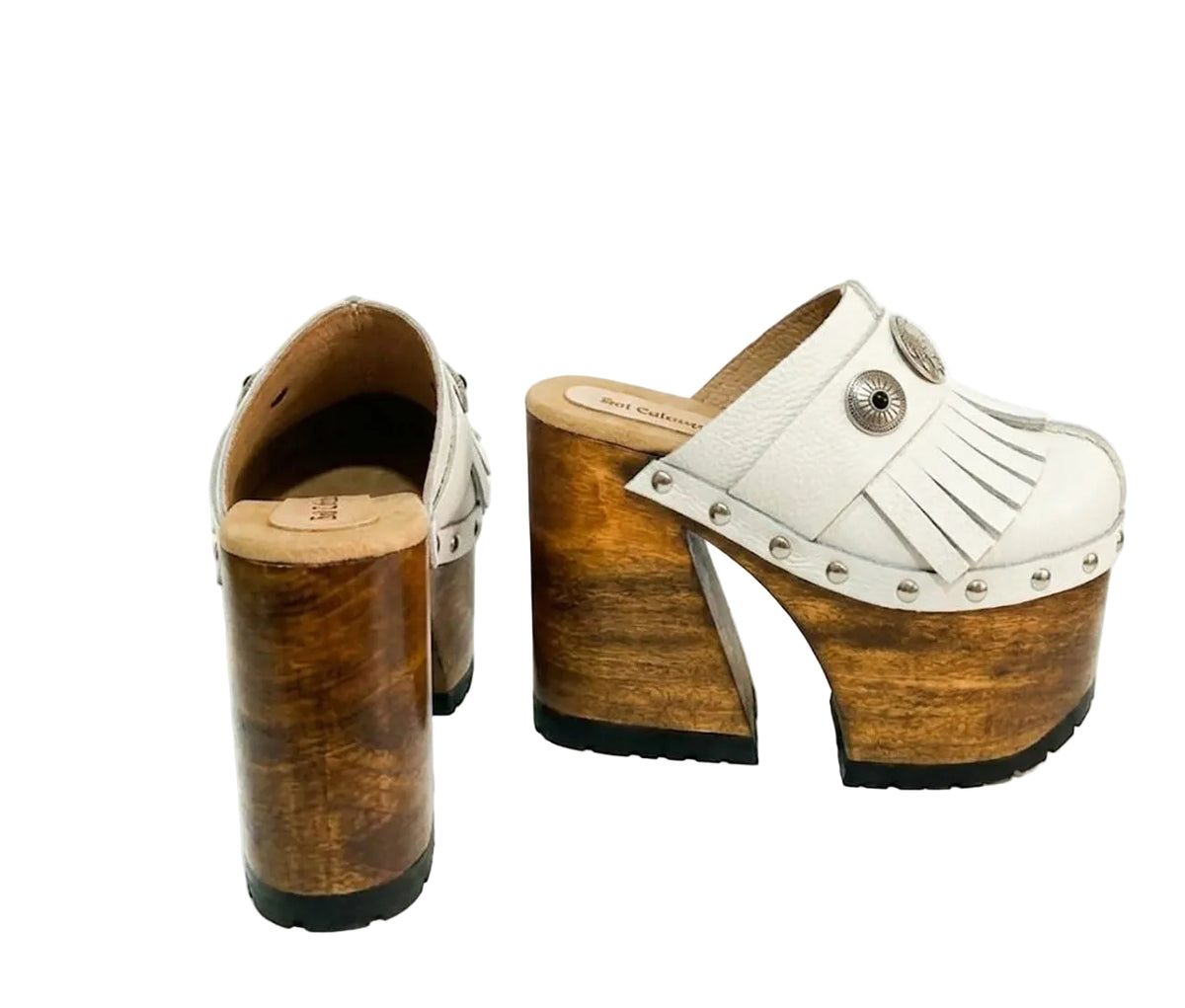 Side view of White Indian Clogs XL featuring extreme 17cm natural wood platform, white leather fringes, and antique silver metal conchos.