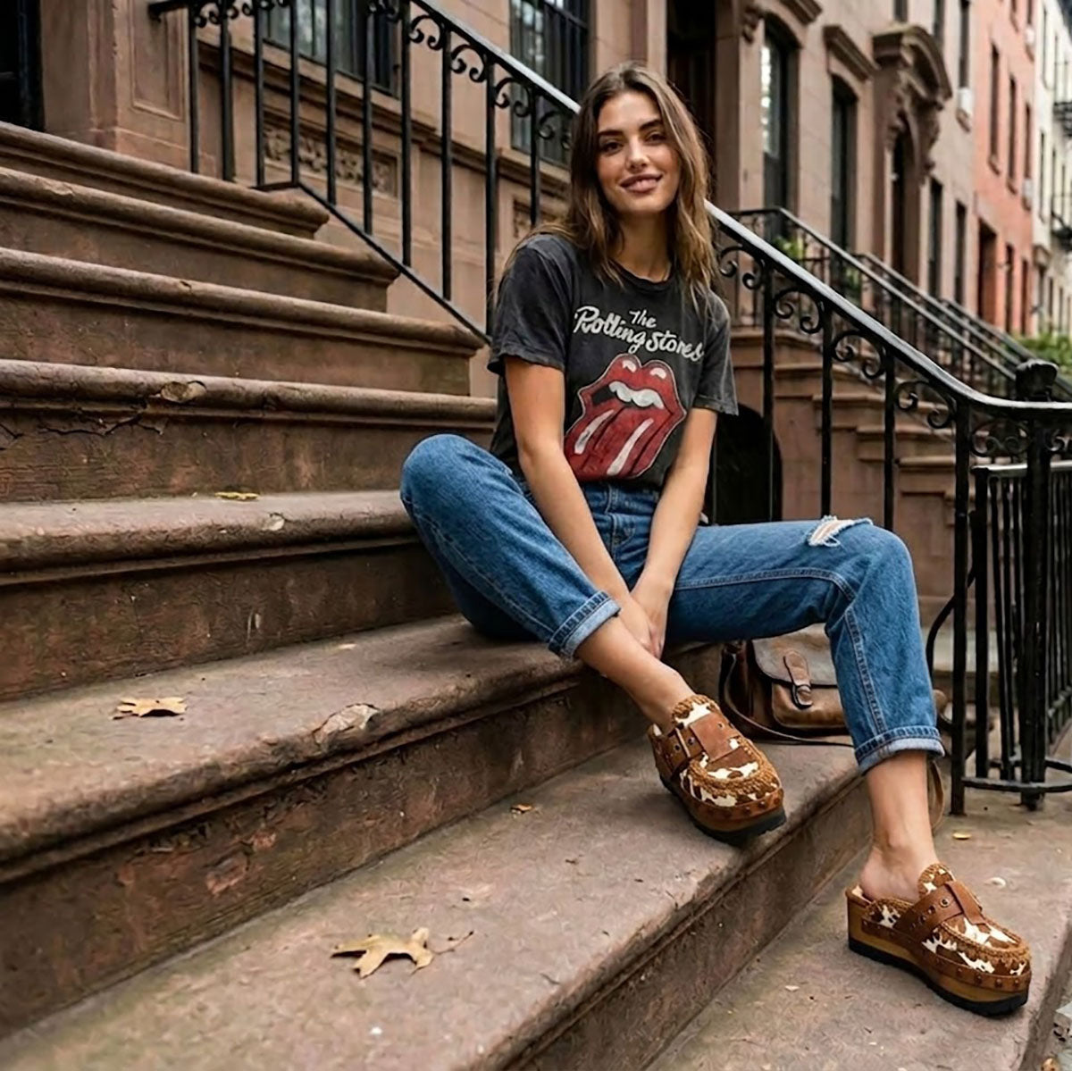 Blogger wearing Oxford Clogs Cowhide Print with jeans and a vintage t-shirt, sitting on city steps for a boho-rock look.