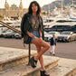Woman sitting outdoors wearing Sol Caleyo Kauai XL platform flip flop sandals in black leather with silver studs, paired with a black leather jacket and denim shorts.