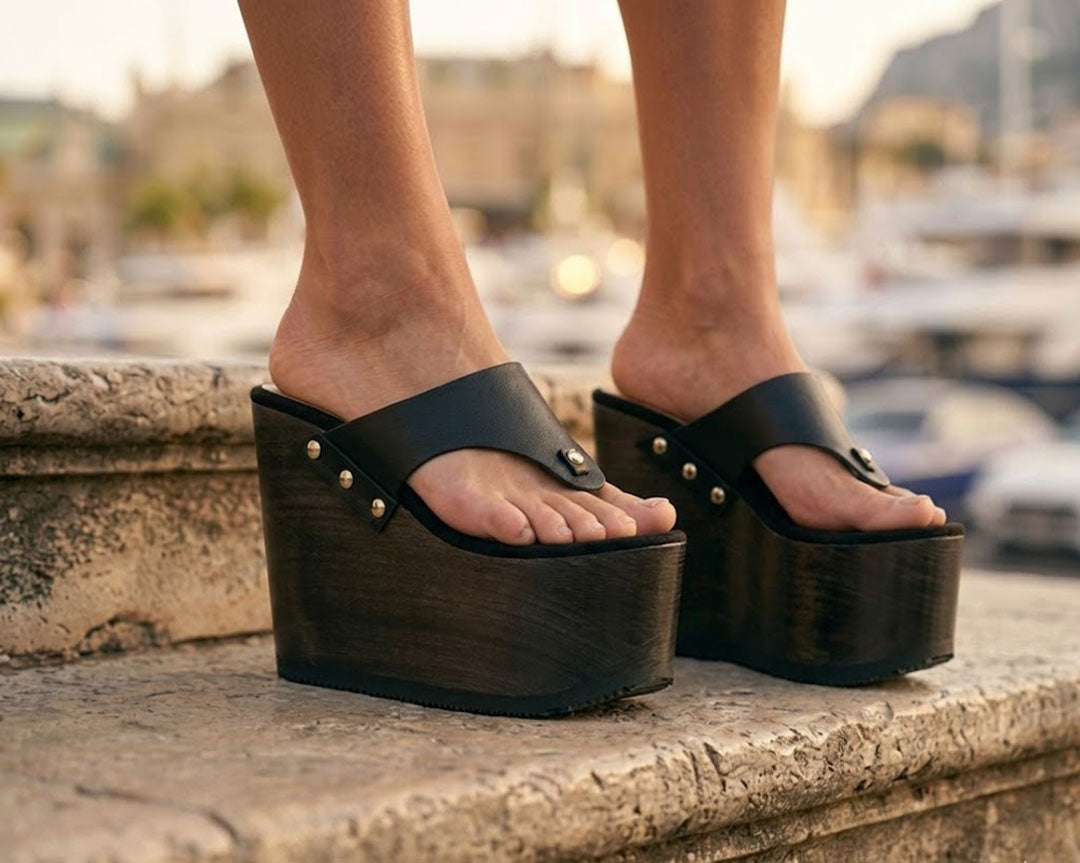 Close-up of a person's feet wearing Kauai XL black leather flip flop sandals with a high wengue wooden wedge platform and silver studs.
