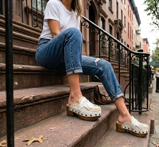 Model wearing white Niza Moccasin Clogs by Sol Caleyo, styled with blue jeans and a white t-shirt for a classic urban bohemian look on city steps.
