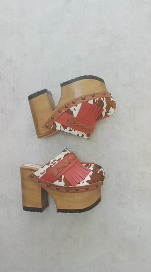 Verona Clogs by Sol Caleyo featuring light brown cow hair leather, red fringe details, and old gold studs on a high wooden platform sole with tractor grip.