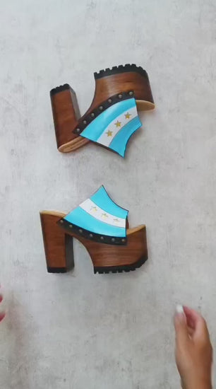 Pair of Sol Caleyo Argentina Sandals featuring a handcrafted wooden block heel and platform, a blue and white leather strap designed as the Argentine flag with three gold stars, and antique gold studs.