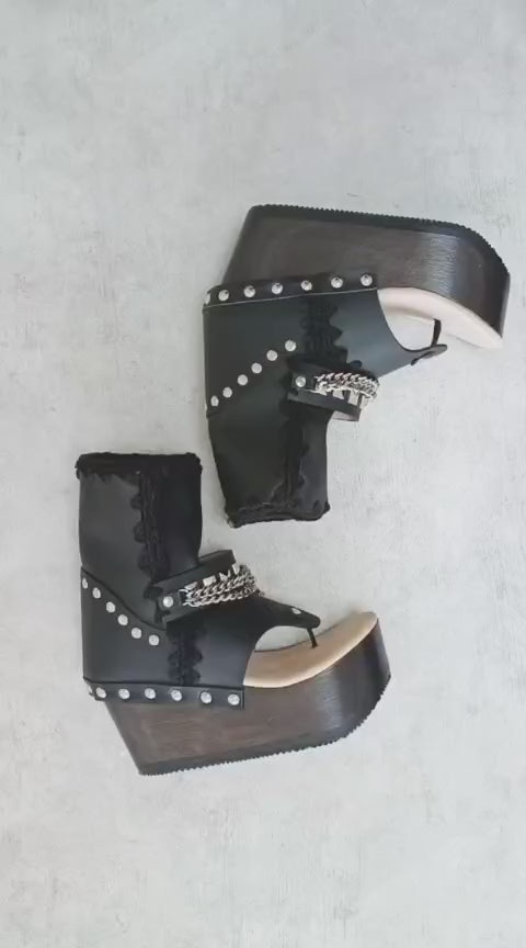 Sol Caleyo Texas Boots: Handcrafted black leather platform flip-flop sandals with wooden wedge heel, silver pyramid studs, and decorative chains. 9cm heel with zig-zag rubber traction sole.