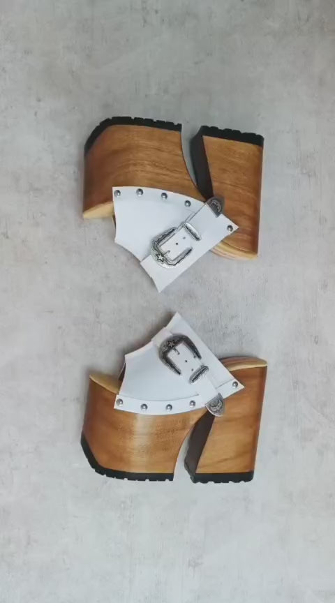 Experience the ultimate statement in bohemian luxury with the Sol Caleyo White Western Sandals. Exclusively handcrafted to order, these extreme platform clogs feature a 17 cm heel and an 11 cm platform, meticulously carved from genuine wood.

Made with premium textured white full-grain leather and adorned with antique silver Western hardware, this nomadic-chic footwear combines high-fashion aesthetics with artisanal durability. Available in sizes 33 to 47.

Key Features:

100% Handcrafted to order (Sustaina
