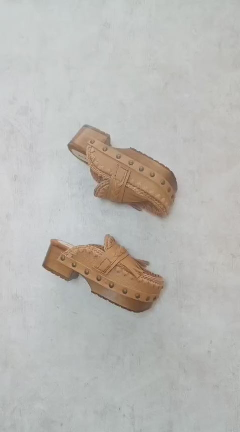 Side profile of Sol Caleyo Niza Clogs in light brown leather, showcasing hand-braided strap, crochet trim, bronze studs, and a sturdy wooden platform sole.