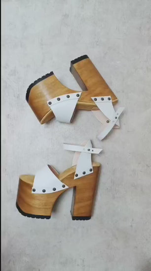 Side view of Crazy White Sandals by Sol Caleyo, featuring white leather straps with bronze studs on a high dark wood platform and tractor sole.