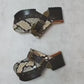Handmade snake print leather clogs with brown leather strap and antique gold buckle on a wooden platform sole.