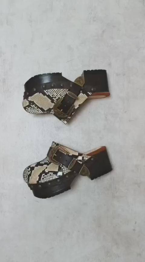 Handmade snake print leather clogs with brown leather strap and antique gold buckle on a wooden platform sole.
