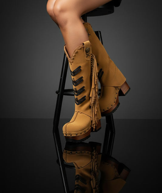 Bohemian fringe cowboy boots by Sol Caleyo worn on model, camel suede leather with black appliqué details and long side fringe, handcrafted wooden platform sole.