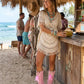 A model wearing the Rhapsody Bohemia Pink Boots at a rustic beach bar. The vibrant pink suede and bohemian details stand out against the sun-drenched wooden deck and coastal decor, embodying a free-spirited summer style.