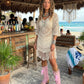 A model wearing the Rhapsody Bohemia Pink Boots at a rustic beach bar. The vibrant pink suede and bohemian details stand out against the sun-drenched wooden deck and coastal decor, embodying a free-spirited summer style.
