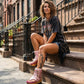 Model wearing the Kenya Flip Flop Pink Boots by Sol Caleyo, featuring metallic pink leather and high wooden platforms in a bright, edgy summer outfit.