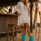 Boho-style model at a beach chiringuito wearing turquoise suede platform flip-flop boots, perfectly complementing a summer beach club outfit.