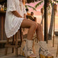 Model at a beach club wearing Atenea beige suede platform boots, showing the natural earthy tones and bohemian details in a sophisticated summer sunset setting