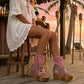 Model wearing Atenea Pink suede platform boots at a beach chiringuito, showcasing the bohemian fringe and shell details in a coastal summer setting.