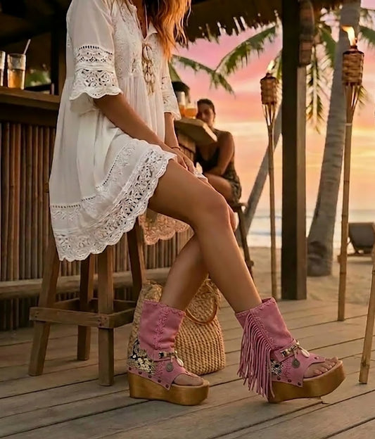 Model wearing Atenea Pink suede platform boots at a beach chiringuito, showcasing the bohemian fringe and shell details in a coastal summer setting.