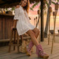 Model wearing Atenea Pink suede platform boots at a beach chiringuito, showcasing the bohemian fringe and shell details in a coastal summer setting.