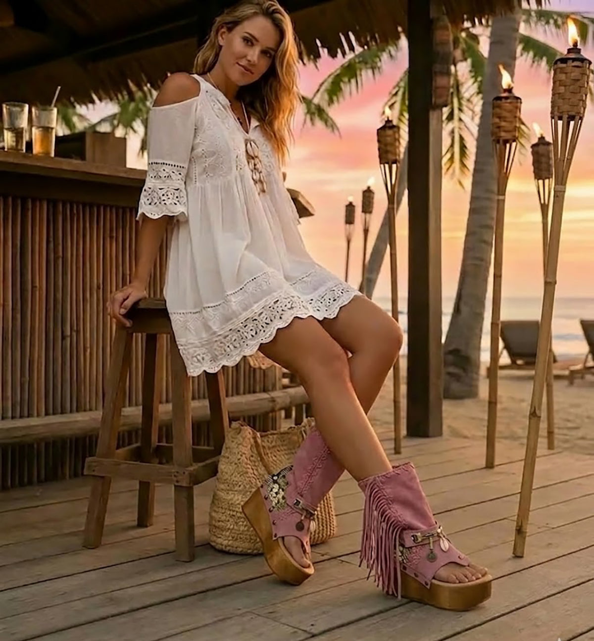 Model wearing Atenea Pink suede platform boots at a beach chiringuito, showcasing the bohemian fringe and shell details in a coastal summer setting.