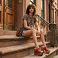 Close-up image of a model from the waist down wearing the Red Luxury Queen Sandals by Sol Caleyo and rolled-up dark denim jeans, posing on a classic brownstone stone staircase in New York City.